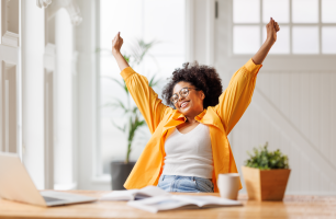 Happy woman joyfully holding up arms in front of a computer