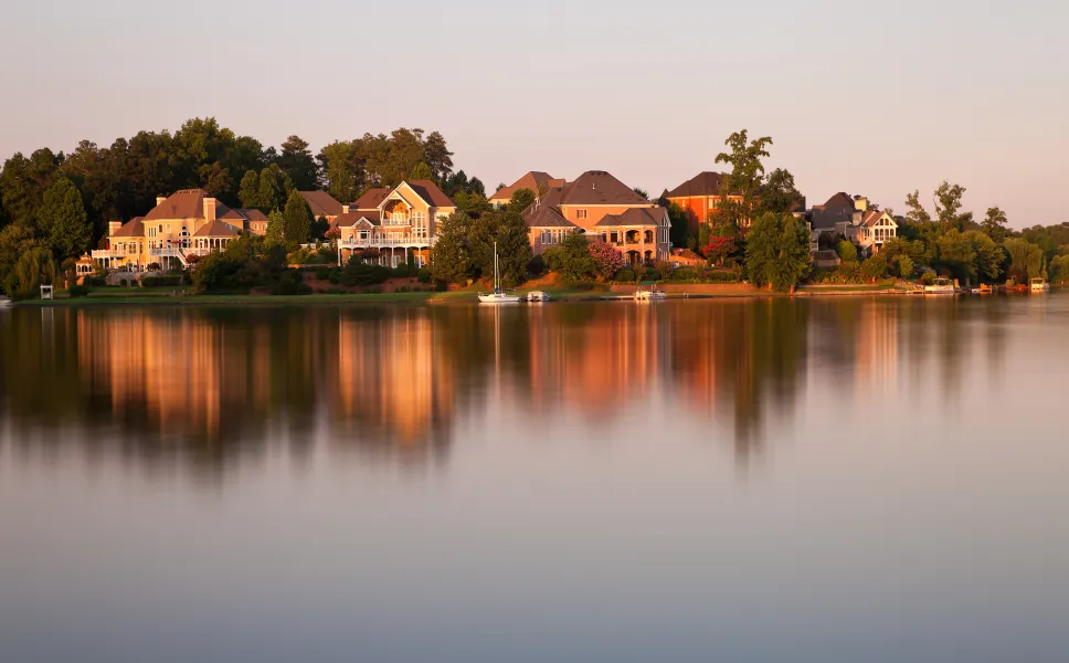 Beautiful scene of houses by the lake surrounded by forests at sunset time